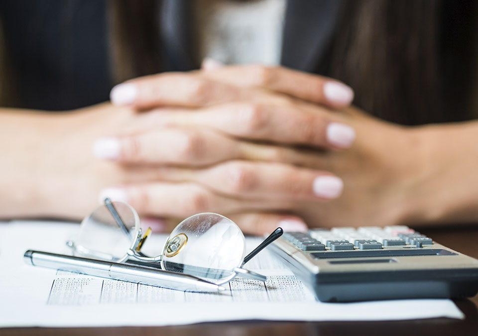 Com mãos cruzadas e calculadora, pessoa analisando entre benefícios e investimentos